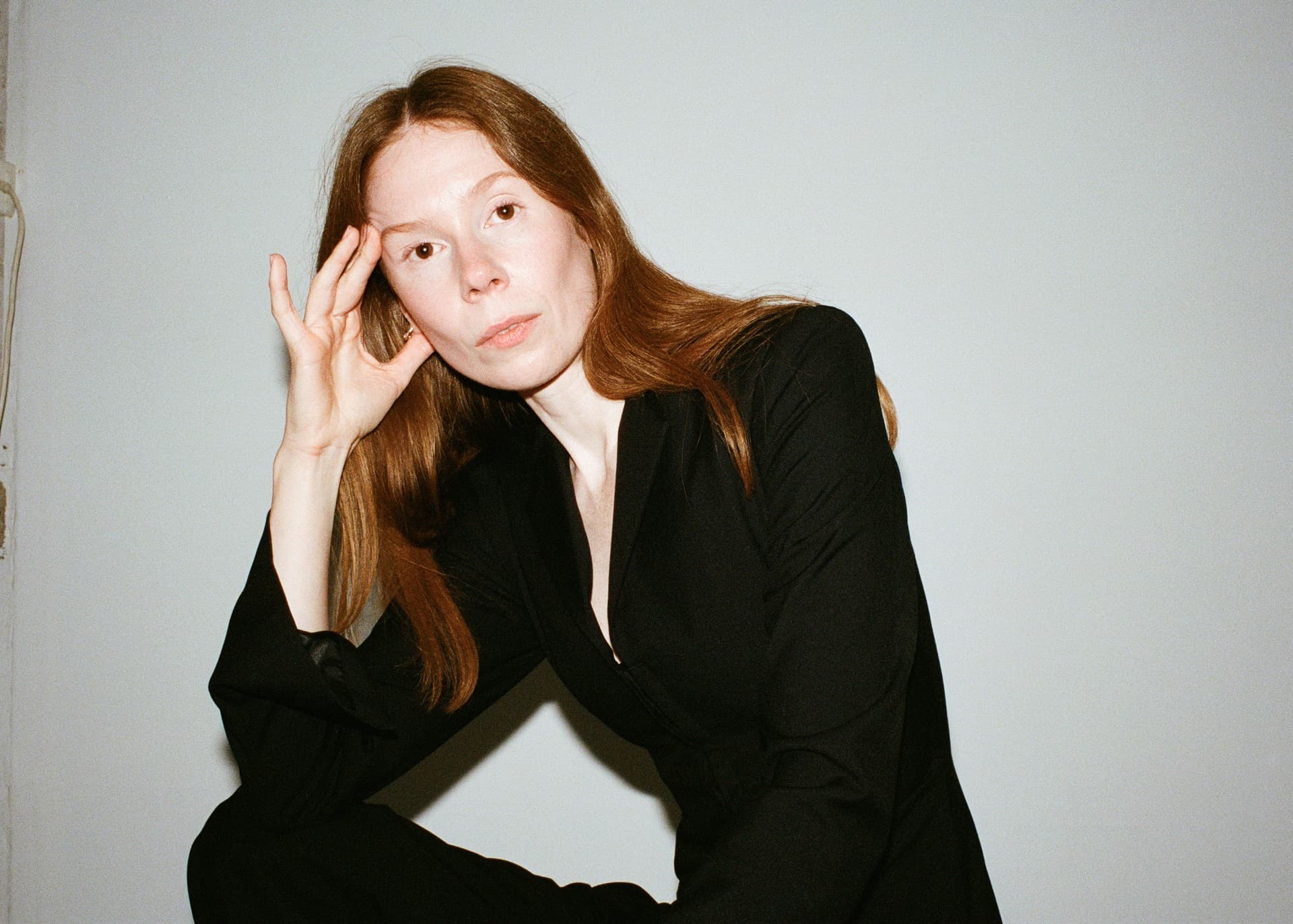 Swedish composer Ylva Fred, with long hair wearing a black outfit, is posing while resting her head on her hand.